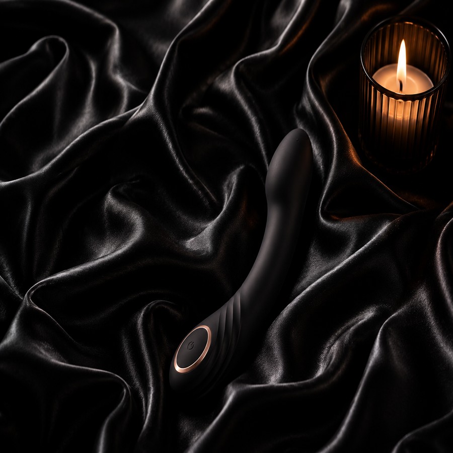 Curved silicone wellness device styled on black satin beside a lit candle